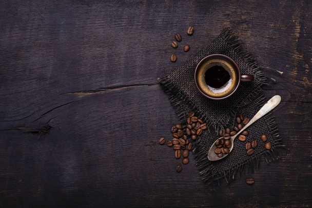 seen from above. On the rough and dark wooden table, a cup of coffee with a spoonful of coffee beans. copy space - Photo, Image