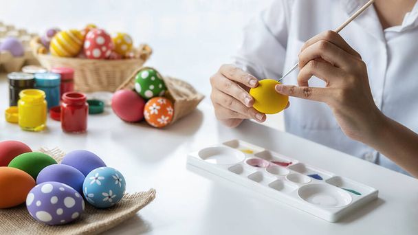 Mujer asiática feliz pintando huevos para Pascua en casa. Familia preparándose para Pascua. - Foto, imagen