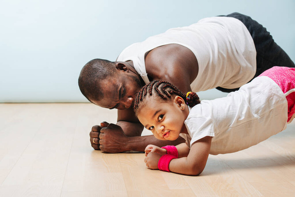 Father and daughter staying in shape in isolation at home, doing plank exercise. Developing their abs. - Photo, image