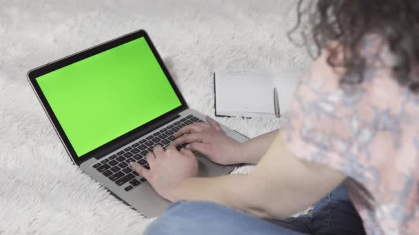 Η νεαρή γυναίκα χρησιμοποιεί ένα φορητό υπολογιστή και πληκτρολογεί στο πληκτρολόγιο, στο χώρο εργασίας στο σπίτι. Το λάπτοπ με την πράσινη οθόνη. Έννοια της τηλεργασίας και της εξ αποστάσεως μάθησης. - Πλάνα, βίντεο