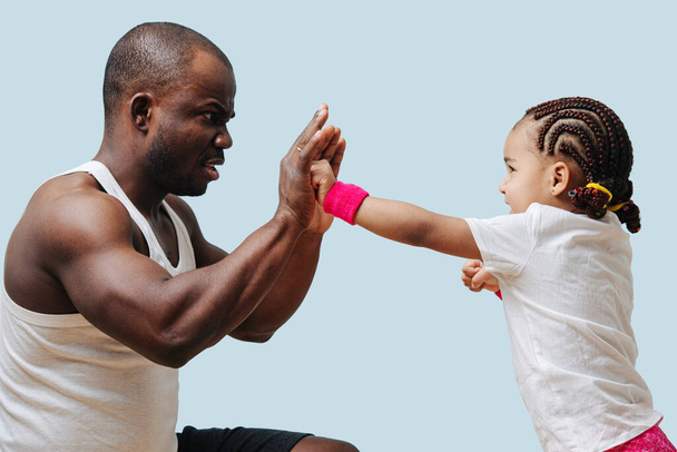 Father training his little daughter to box, making serious face. She punches enthusiastically. Over blue - Photo, Image