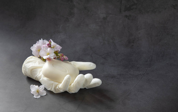 Uma luva protetora médica com um pedaço de sabão e flor de cereja no fundo escuro
 - Foto, Imagem