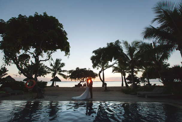 Silhouettes of the bride and groom at sunset. The reflection in the pool. - Fotografie, Obrázek