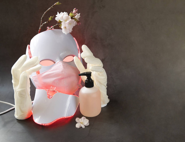 Χρωματοθεραπεία μάσκα λαμπερό κόκκινο με προστατευτική μάσκα, γάντια, ένα μπουκάλι σαπούνι και άνθη κερασιάς - Φωτογραφία, εικόνα