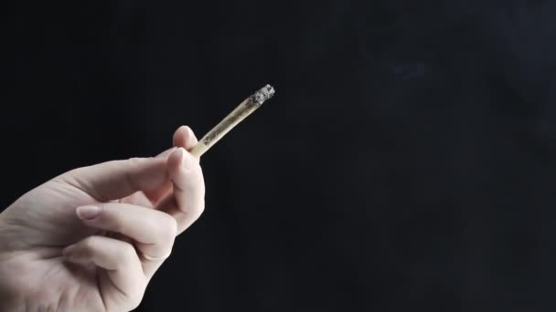 Großaufnahme einer weiblichen Hand mit medizinischem Marihuana-Joint und Rauchen auf schwarzem Hintergrund, Zeitlupe. Cannabis ist ein Konzept der pflanzlichen oder alternativen Medizin - Filmmaterial, Video