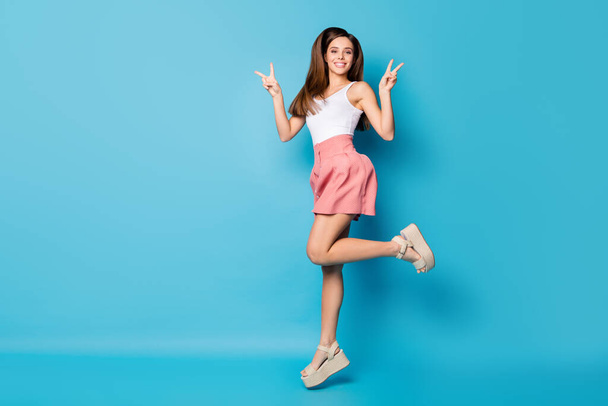 Full size photo of cheerful cute pretty girl jump make v-sign enjoy spring free time weekend holiday wear good look singlet isolated over blue color background - Fotoğraf, Görsel