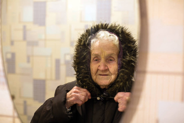 Eine ältere Frau spiegelt sich im Spiegel und trägt Winteroberbekleidung. - Foto, Bild