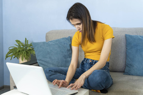 Woman which sitting at the sofa indoors in home office. Working from home a laptop computer - Φωτογραφία, εικόνα