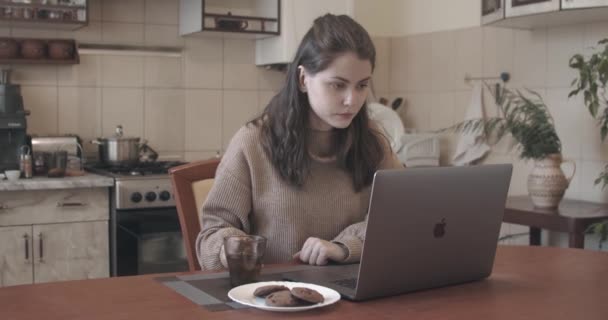 Attractive woman working from home on a laptop computer in domestic kitchen - Imágenes, Vídeo