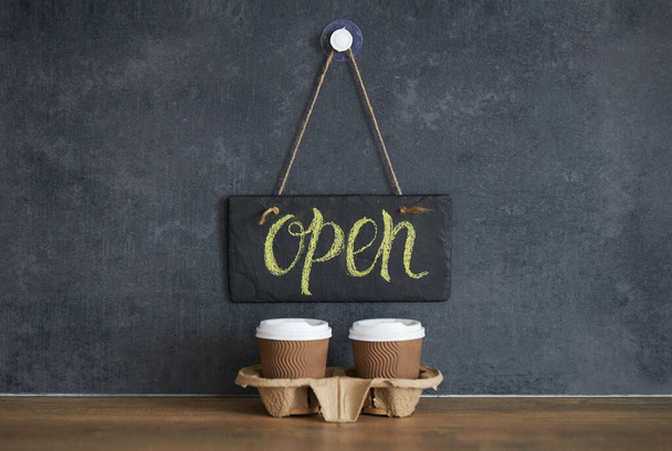 A sign that says Open on cafe, on a black chalk board. After quarantine. Takeaway coffee glasses on dark background. Business opening - Photo, Image