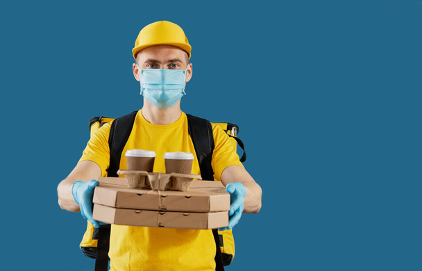 Courier in protective mask and medical gloves delivers takeaway food and coffee. Delivery service under quarantine. Copy space for text - Foto, Bild