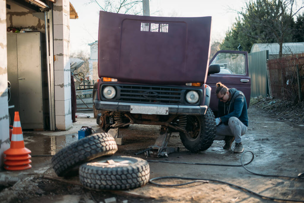 Человек ремонтирует машину, ставит колеса, меняет сезонные шины. Молодой парень сам ремонтирует машину, ставит новые колеса в частный гараж - Фото, изображение