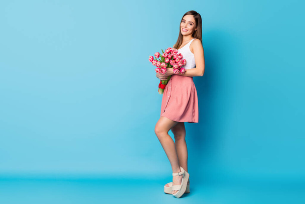 Full size profile side photo of attractive lady hold tulips bouquet she get on 8-march 14-february celebration wear white style singlet footwear isolated over blue color background - Фото, зображення