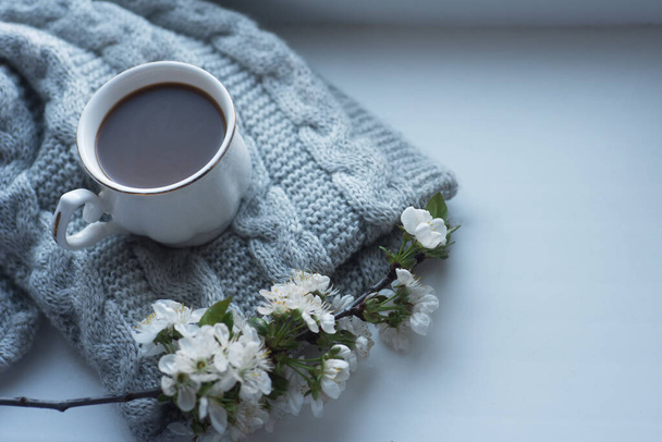 The composition consists of a cup of aromatic coffee with milk, a tweed of flowers and a wool knitted scarf on the window. Photo in daytime lighting. - Фото, зображення