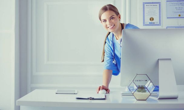 Portrait of female physician using laptop computer while standing near reception desk at clinic or emergency hospital - Zdjęcie, obraz