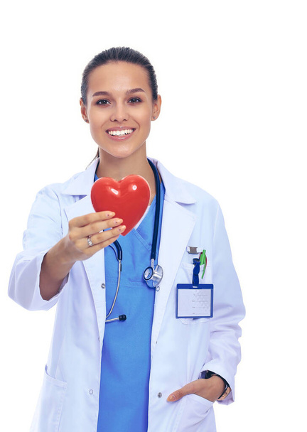 Positive female doctor standing with stethoscope and red heart symbol isolated - Zdjęcie, obraz