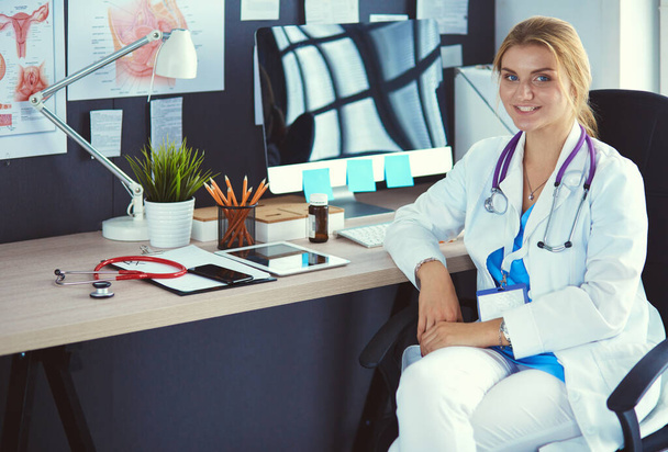 Beautiful young smiling female doctor sitting at the desk - Fotó, kép