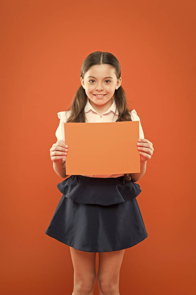 attention please. school girl hold paper on orange background. copy space. happy little girl in school uniform with add. useful information. back to school. look here. writing notes. modern education - Fotó, kép