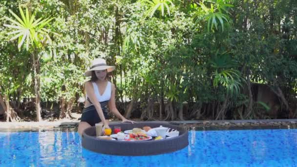 záběry mladé asijské ženy šťastný úsměv vychutnat s plovoucí snídaně tác v bazénu v hotelovém resortu - Záběry, video