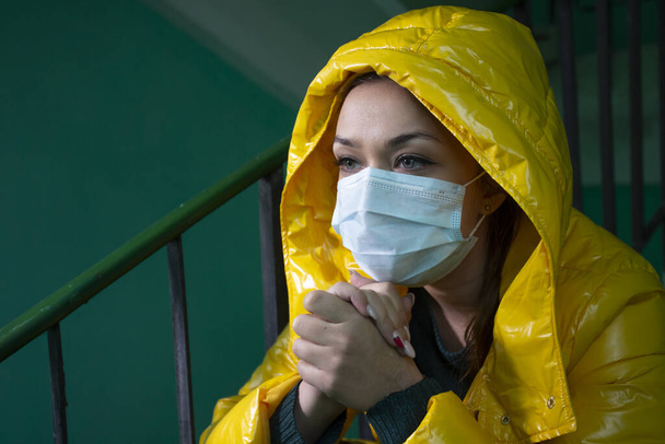 Biała dziewczyna w masce medycznej w opuszczonym budynku siedzi i odwraca wzrok - Zdjęcie, obraz