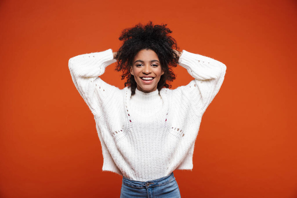 Beautiful cheerful young african woman wearing sweater standing islolated over red background - 写真・画像