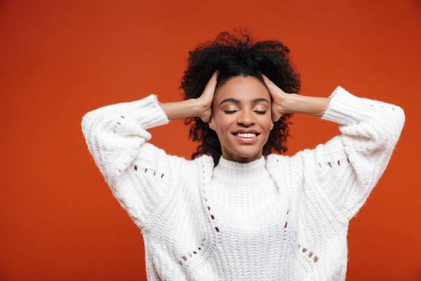 Beautiful cheerful young african woman wearing sweater standing islolated over red background, eyes closed - Foto, immagini