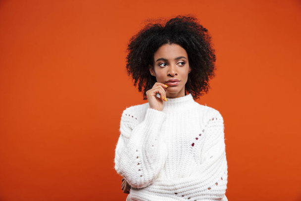 Pensive young african woman wearing sweater standing isolated over red background, looking away - Foto, Bild
