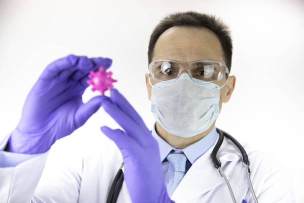 Лаборант в защитной маске и очках держит коронавирусную клетку
 - Фото, изображение