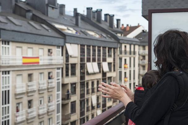 een moeder en haar baby applaudisseren vanaf het balkon uit solidariteit met het gezondheidspersoneel dat de covid-19 geneest - Foto, afbeelding