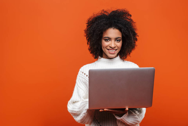 Attractive smiling young african woman standing isolated over red background, using laptop computer - Fotoğraf, Görsel
