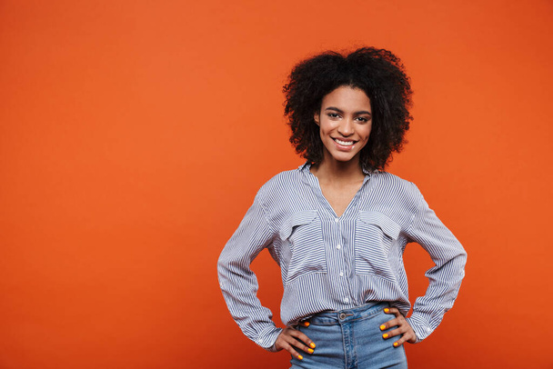 Smiling young attractive african woman wearing casual clothes standing isolated over red background, posing - Zdjęcie, obraz