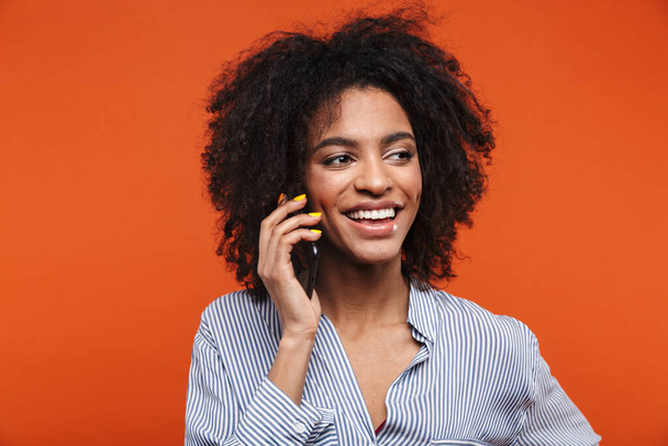 Smiling young attractive african woman talking on mobile phone isolated over red background - Foto, Bild