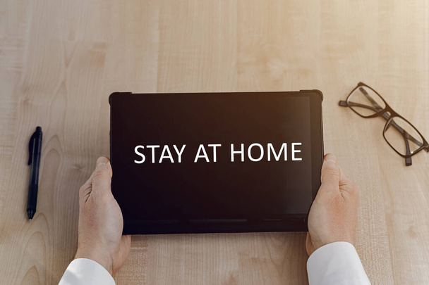 Man holding a tablet with a message that says 'Stay at home'. Tablet, pen and glasses on table.Home office, online education, stay home business concept. Stay home save lives Pandemic Covid-19. - Photo, Image