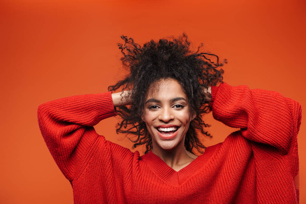 Beautiful cheerful young african woman wearing sweater standing islolated over red background - Foto, Bild