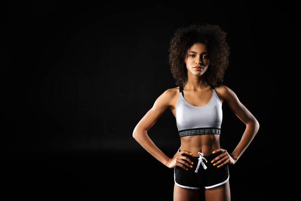 Image of young african american woman in sportswear posing with hands on waist isolated over black background - Фото, зображення
