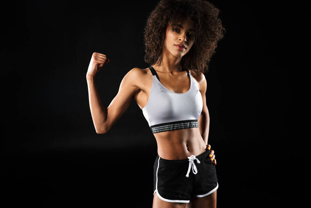 Image of young african american woman in sportswear posing and showing her bicep isolated over black background - Valokuva, kuva