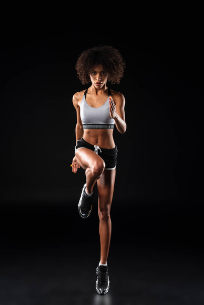 Image of athletic african american sportswoman doing exercise while working out isolated over black background - 写真・画像