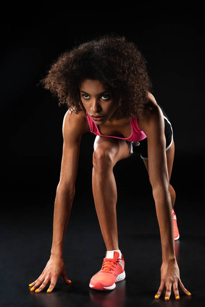 Image of athletic african american sportswoman doing exercise while working out isolated over black background - Фото, изображение