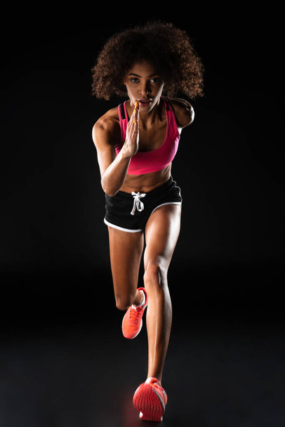Image of athletic african american sportswoman running while working out isolated over black background - Photo, Image