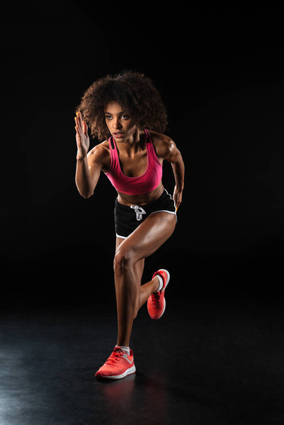 Image of athletic african american sportswoman running while working out isolated over black background - Foto, Bild