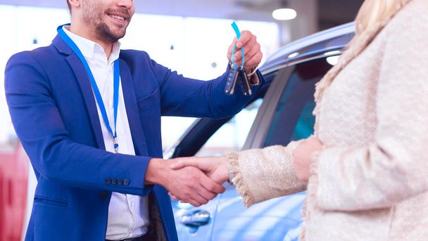 Car salesman sells a car to happy customer in car dealership and hands over the keys. - Foto, immagini