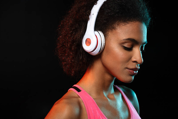 Image of pleased african american woman posing and using headphones isolated over black background - Фото, зображення