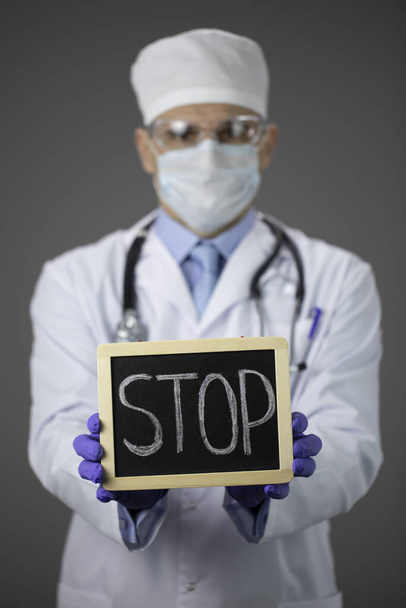 Tıbbi üniformalı erkek doktor, koruyucu maske ve elinde dur işareti olan gözlük. - Fotoğraf, Görsel