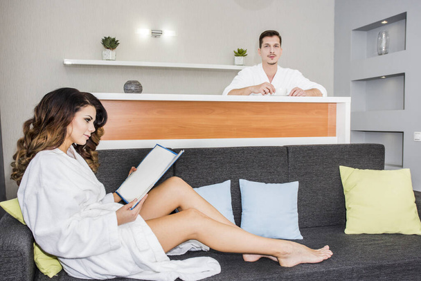 Симпатична сексуальна дівчина в халаті вивчає послуги спа-готелю, молода пара відпочинку
 - Фото, зображення