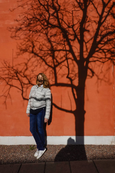 Stockholm, Sweden   A woman stands against a wall in Nybodyhojden with a tree shadow. - Photo, Image