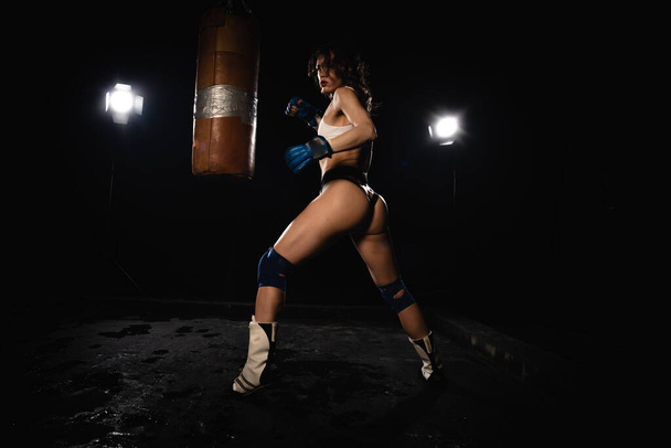 Young sexy Woman boxer. Martial arts or self defence. Sport boxer woman in boxing gloves makes a kick . Fitness girl training kick boxing. Boxing training on ring. Confident athlete woman in boxing gloves. Sport and fitness. Silhuette on black backgr - Foto, imagen
