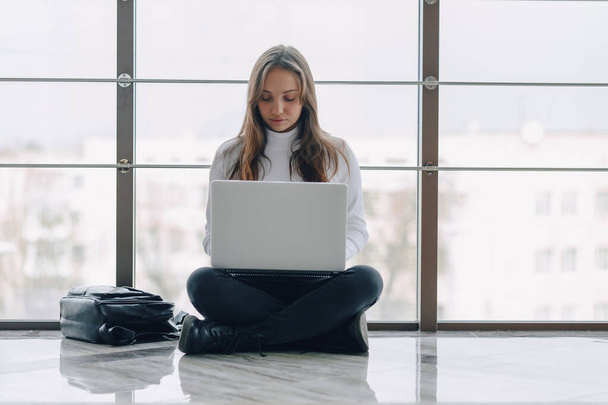 attractive girl working with laptop and things in airport terminal or office on floor. travel atmosphere or alternative work atmosphere. freelancer student travels to business meeting. concept of alternative workplace, technology and waiting. - Photo, Image