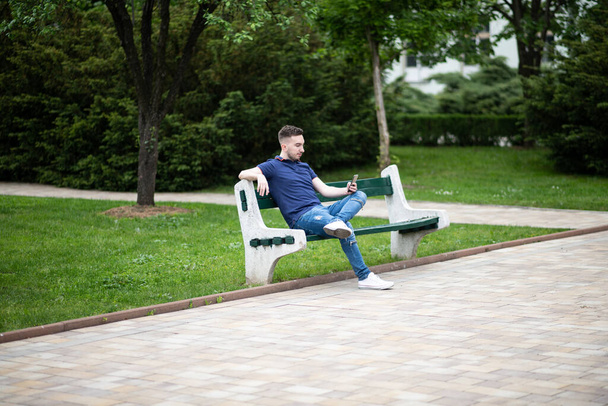 Portrait of a Confident and Successful Young Man With Blue Shirt Outside in Park Sitting on Bench - Foto, Imagem