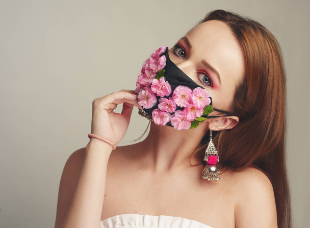 Girl with gorgeous long hair in an antiviral mask. Fashion photo on the cover of the magazine. Pandemic, virus, coronavirus, masked girl spring has come. Spring fashion, model in a mask of flowers - Photo, Image