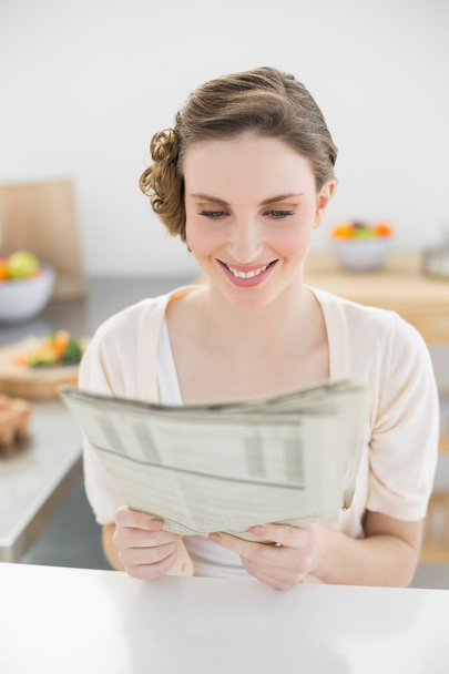 Fresh young woman reading newspaper sitting in her kitchen - Photo, image